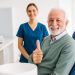 Older male dental patient smiling and giving a thumbs-up while sitting in a dental chair, with a female dental professional standing behind him in a bright, modern clinic.