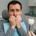 Man looking anxious in a dental chair while a dentist shows him a dental implant model.